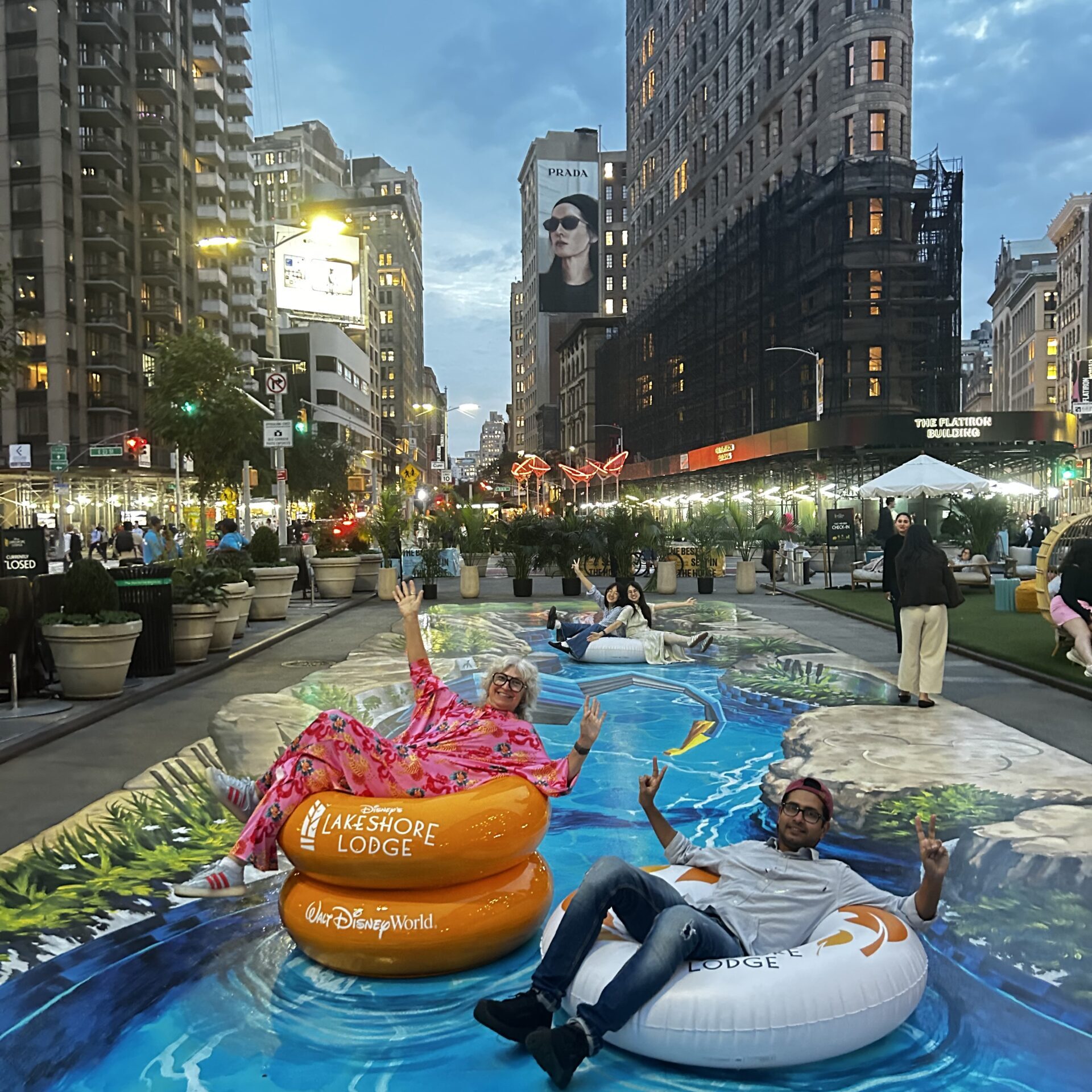 Interactive 3D lazy river street painting by Tracy Lee Stum at Flatiron Plaza in Manhattan, NYC, with visitors posing on inflatable tubes.